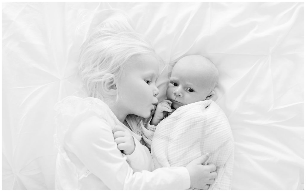 black and white big sister kissing newborn brother